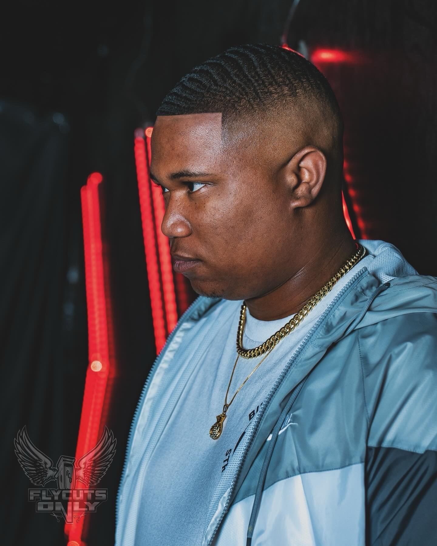 A FLYCUTS0NLY client in profile under red neon, waves and a razored temple line